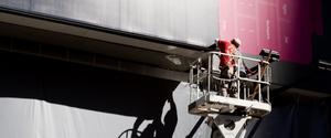 A man in a mechanized basket doing work on a billboard