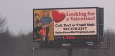 A somewhat grainy photo of a digital billboard that shows a man with a chainsaw standing in an equipment room. The ad asks "Looking for a Valentine?" and then offers contact information for people to get in touch with Matt.