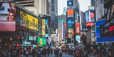 A busy New York street, digital billboards up on the buildings on either side of the road.