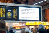 A photo of a large digital sign in London's Victoria Station. On the screen is the question "who is the most beautiful woman in your life? why?"